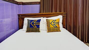 Una cama con dos almohadas decoradas con un diseño de flecha azul y amarilla, un cabecero de madera y paredes con azulejos morados.