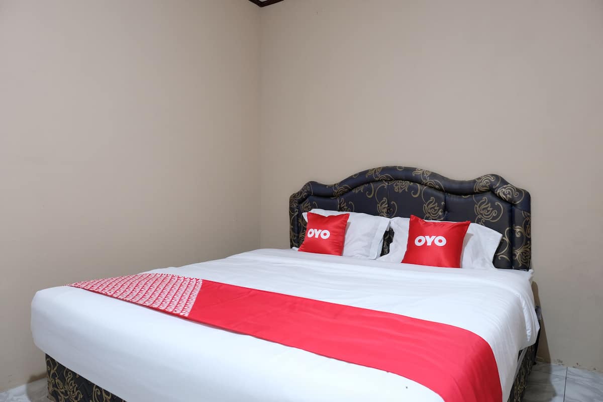 A neatly made bed with a red and white bedspread, two red pillows with the word "OYO" on them, and a dark headboard with a decorative pattern.