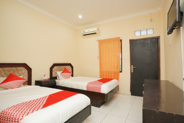 A hotel room with two beds, a wooden headboard, an air conditioner, a door, and a TV mounted on the wall. - OYO 2003 Female Guest House (Probolinggo)