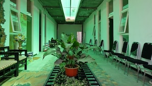 A hallway with a greenish tint, featuring a central potted plant, chairs, and a tiled floor. - OYO 1622 Kakap 88 Family Homestay (Malang)