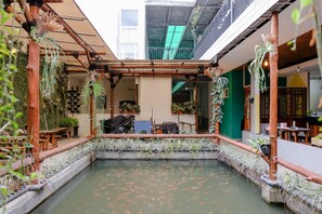 A courtyard with a koi pond, bamboo structures, and potted plants. - OYO 1622 Kakap 88 Family Homestay (Malang)