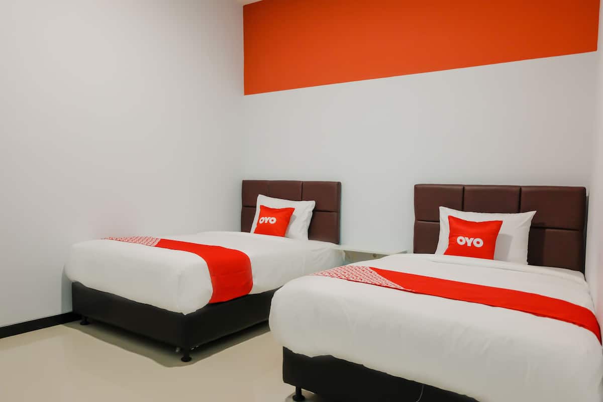 Two beds with white and red bedding, a brown headboard, and a red accent wall.