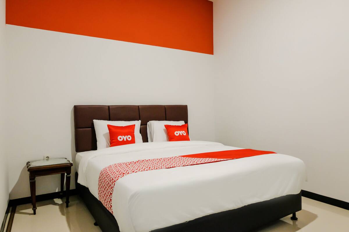 A hotel room with a bed, a nightstand, and a red and white patterned bedspread.