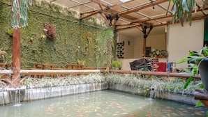 An indoor koi pond with a bamboo structure overhead and a green wall with plants. - OYO 1622 Kakap 88 Family Homestay (Malang)