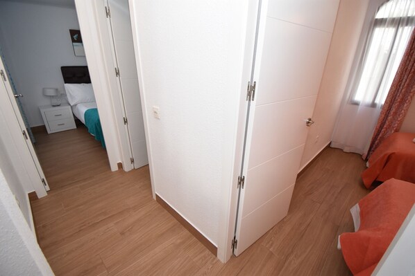 A bedroom with a wooden floor, a bed with a teal blanket, a white wardrobe, and a red chair.