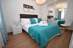A modern hotel room with a large bed, a bedside table, a chair, and a mirror.