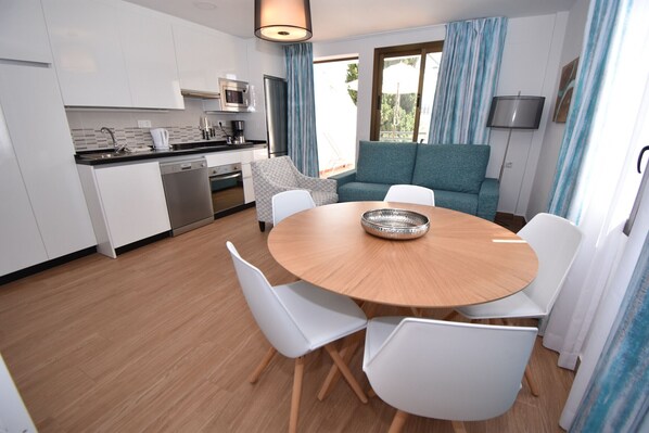 A modern kitchen with white cabinets, a dining table with white chairs, and a blue sofa.