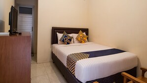 Une chambre à coucher avec un lit, des oreillers, un téléviseur posé sur un meuble et une fenêtre.