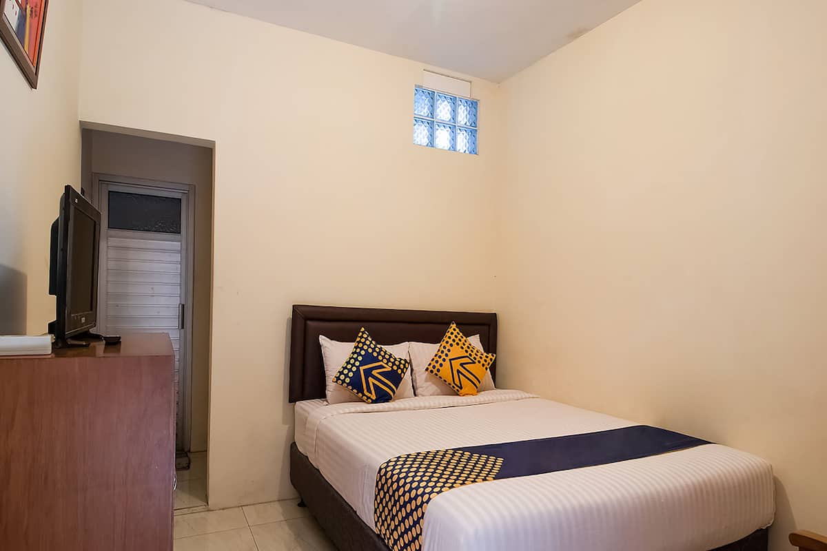 A bedroom with a bed, pillows, a TV on a stand, and a window.