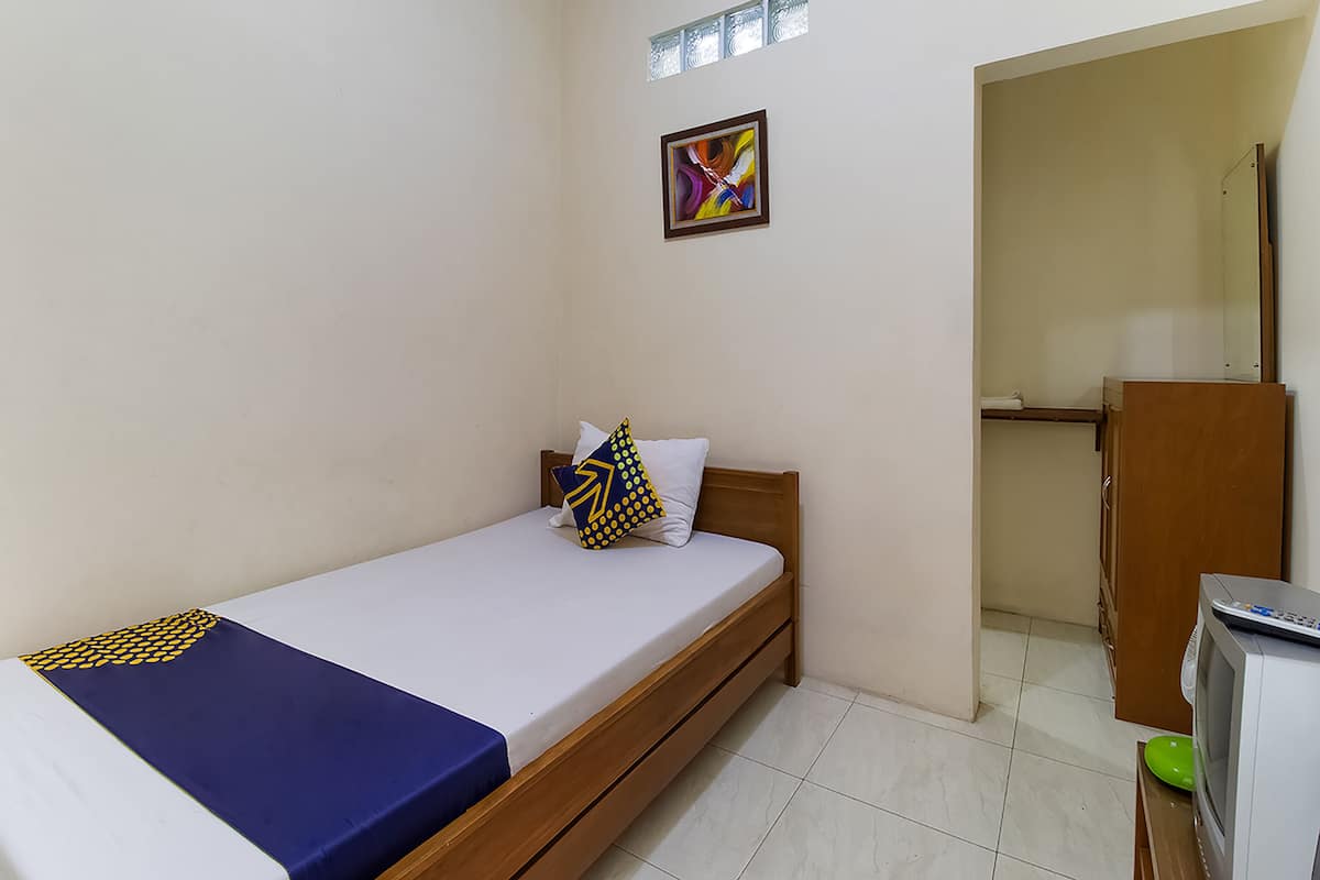 A small, clean room with a single bed, a wooden wardrobe, and a television.