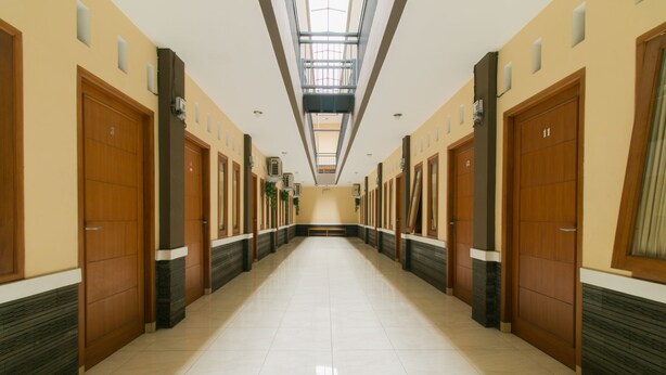 Un long couloir bien éclairé, avec des portes en bois numérotées 11 et 12, qui mène à un espace central doté d’une verrière.