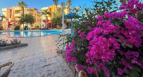 A swimming pool with lounge chairs, a gazebo, and bougainvillea flowers.