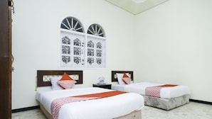 A hotel room with two beds, a window with decorative grills, a wooden headboard, and a tiled floor. - Hotel O Penginapan Bidara Syariah (Probolinggo)