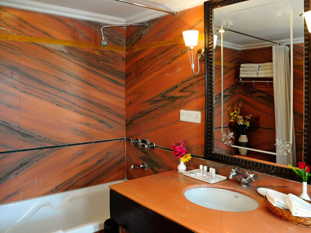 A bathroom with a marble wall, a sink with toiletries, and a mirror.