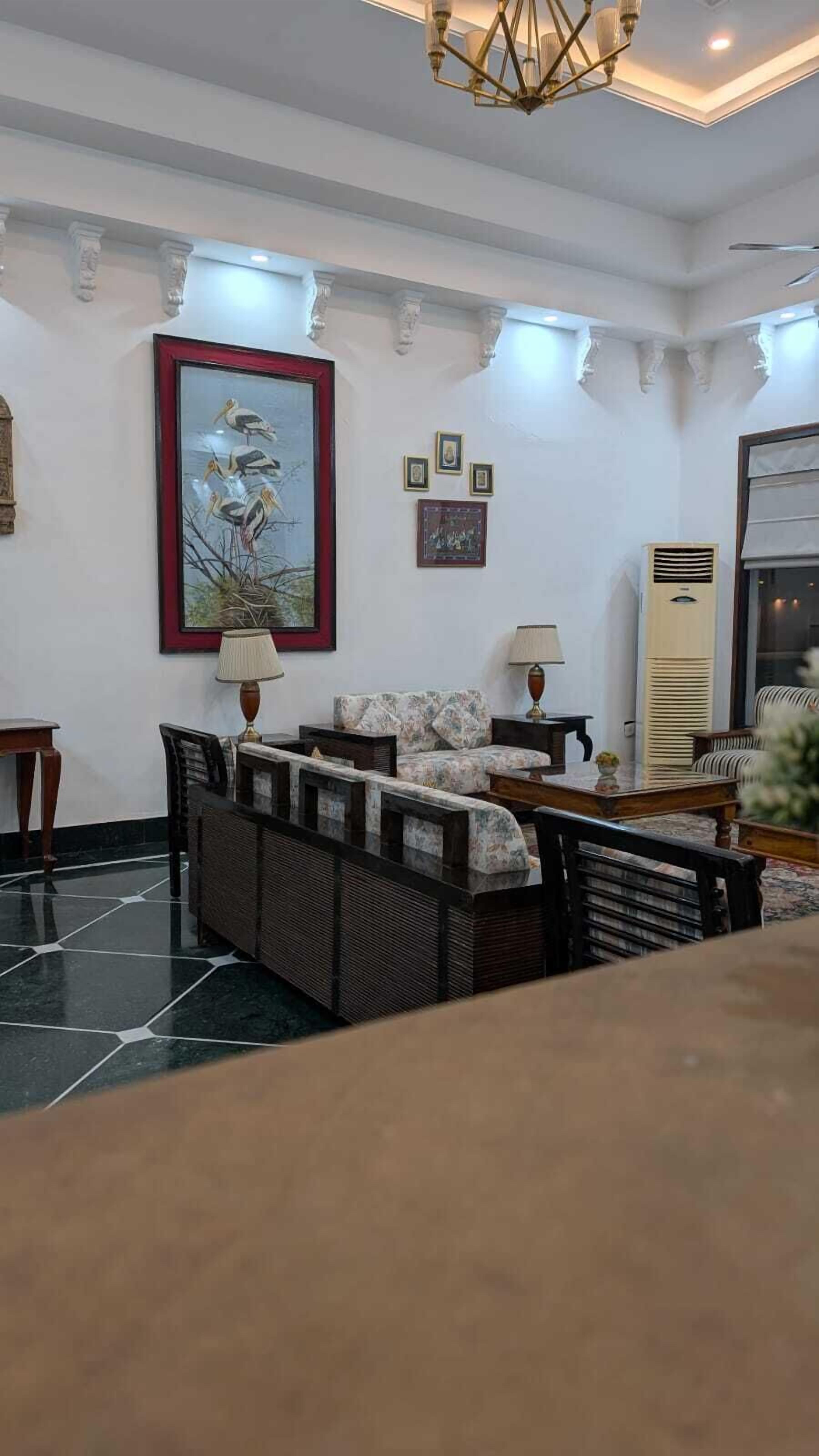 A spacious living room with a large sofa set, a painting of birds, and a modern chandelier.