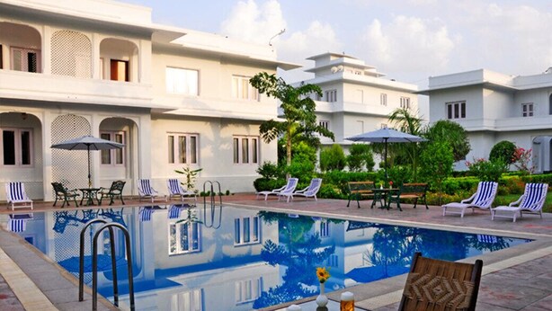 A pool area with lounge chairs and umbrellas, surrounded by a building with traditional architecture.
