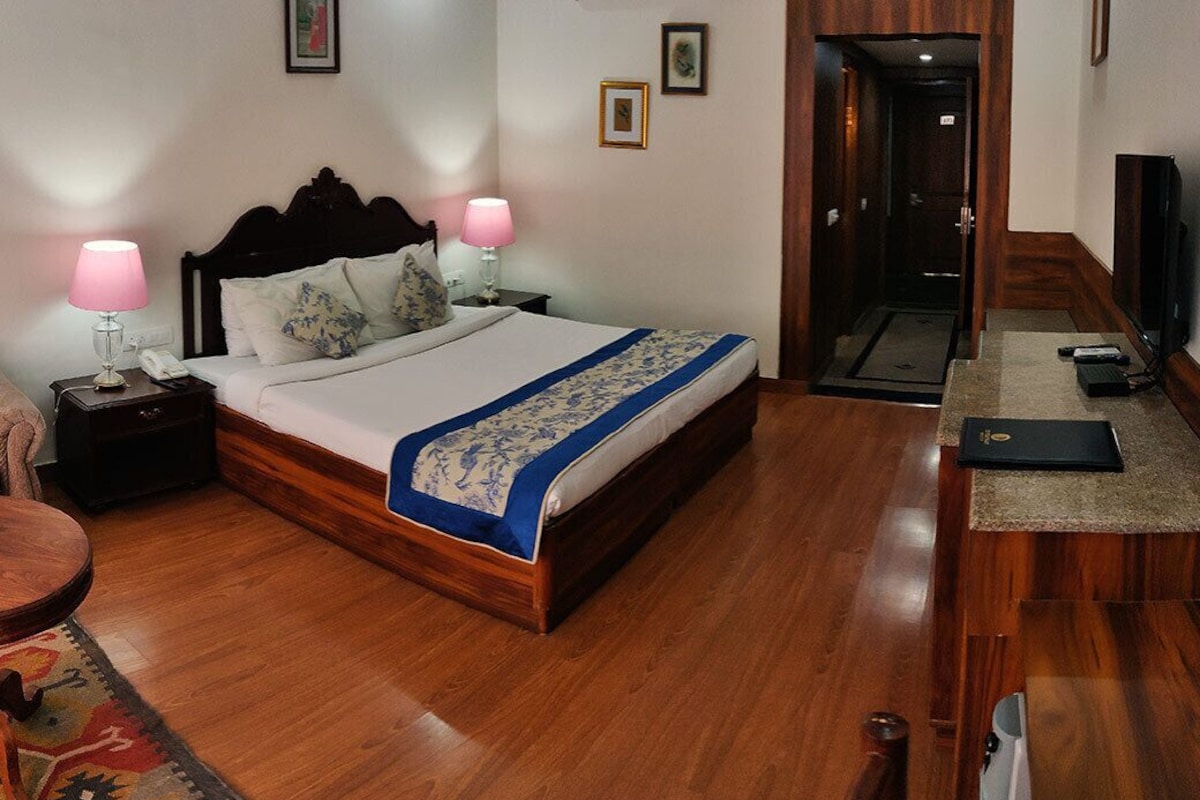 Una habitación de hotel con una cama de madera, lámparas de noche, un escritorio con silla y un televisor.