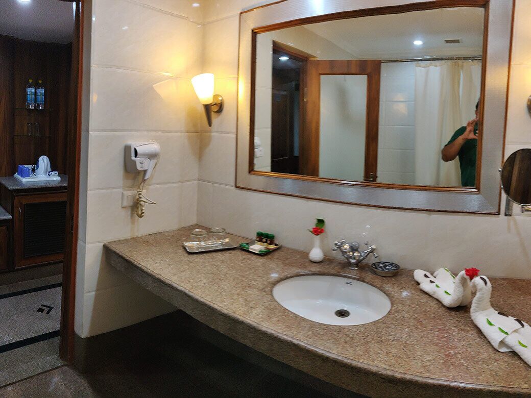 A bathroom with a granite countertop, a white sink, a mirror, a towel rack with a towel, a soap dispenser, and a hand dryer.
