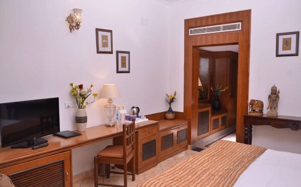 Una habitación de hotel con un escritorio de madera, televisión, cama y espejo.