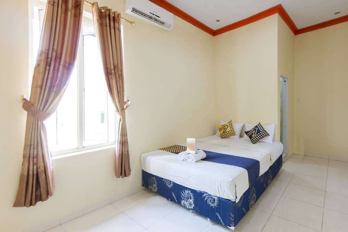 Une chambre d’hôtel avec un lit, des rideaux, un appareil de climatisation et une fenêtre.