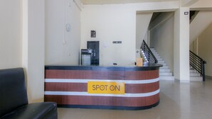 A reception desk with a sign reading "SPOT ON" in a hotel lobby with a staircase and a black leather chair. - Hotel O Pondok Bintang (Somba Opu)