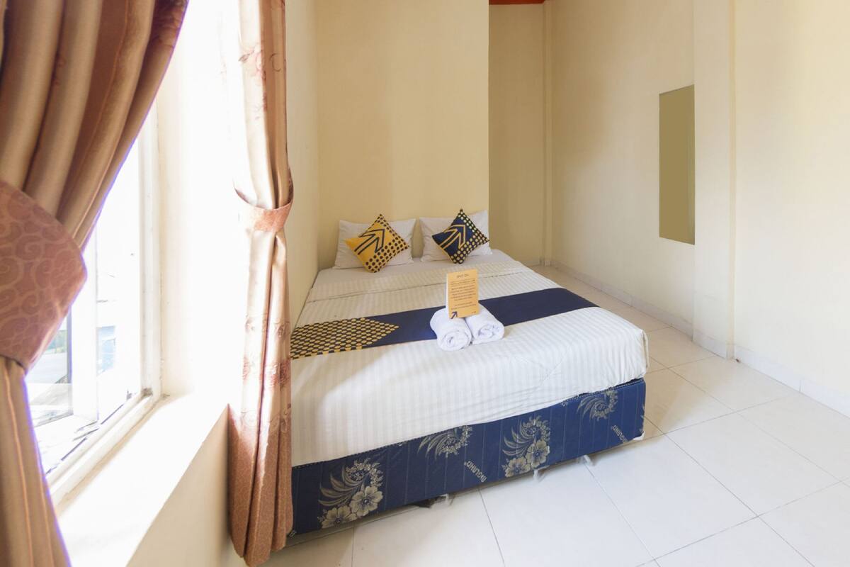 Une chambre d’hôtel avec un lit, des oreillers, un panneau et une fenêtre avec des rideaux.