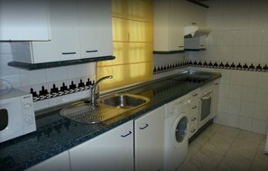 Cozinha com armários brancos, pia, máquina de lavar e micro-ondas.