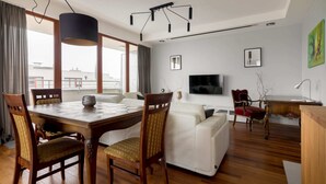 A modern living room with a wooden dining table, white sofa, and a TV mounted on the wall. - Hlonda Deluxe Apartment with Terrace (Warsaw)