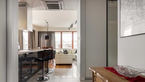 A modern kitchen with a bar area, a dining table, and a sofa in the background. - Hlonda Deluxe Apartment with Terrace (Warsaw)