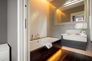 A modern bathroom with a large bathtub, a vanity with a mirror, and a wall-mounted light fixture.