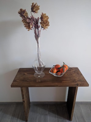 Ein Holztisch mit einer klaren Glasvase, in der getrocknete Blumen und eine Schale Orangen stehen.