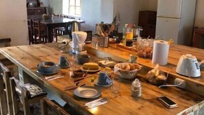 Une table de salle à manger en bois, avec des chaises, une machine à café et divers aliments pour le petit-déjeuner.