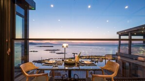 Un comedor con una mesa lista para dos personas, con vista a un cuerpo de agua, tierra distante y cielo despejado.