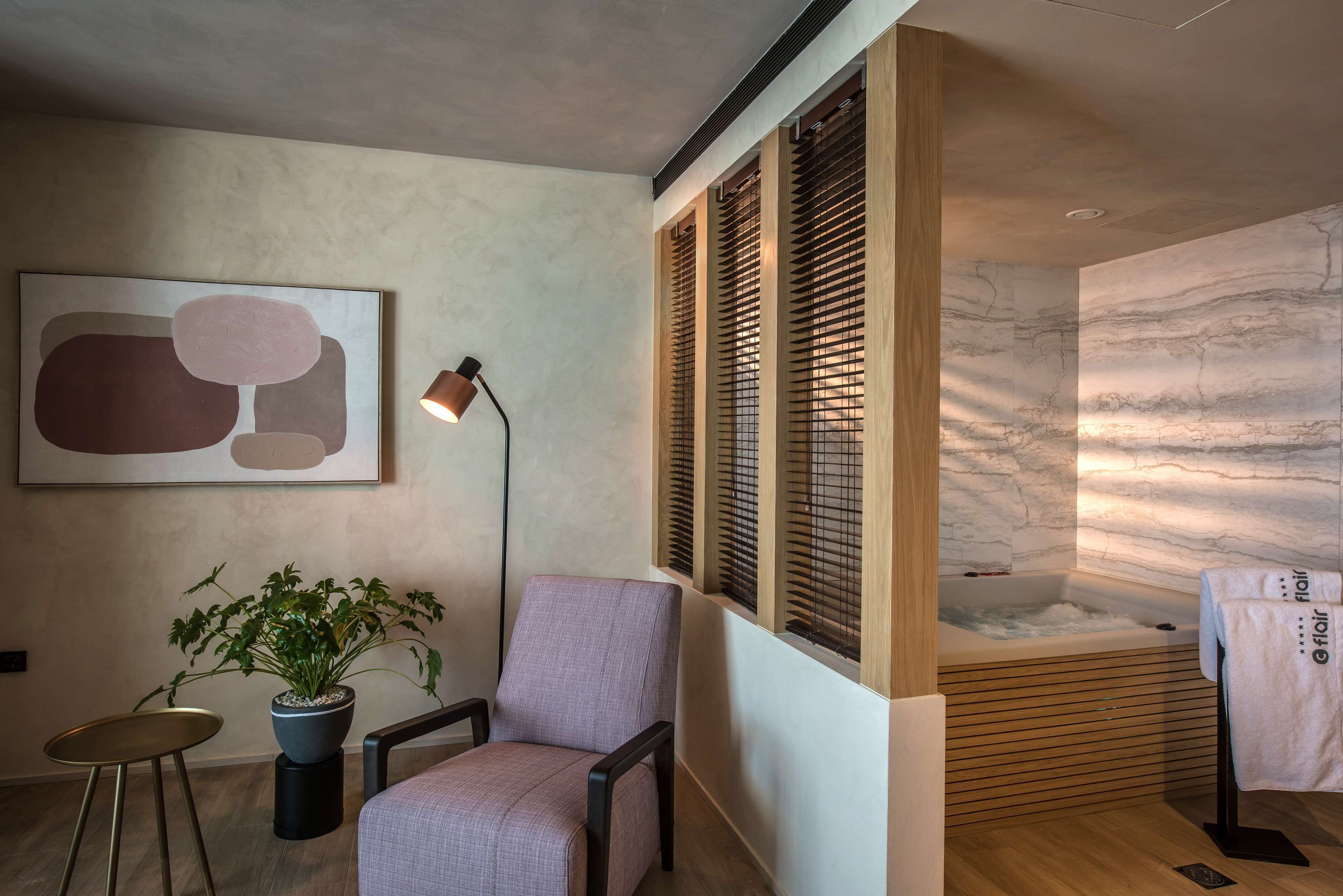 A modern bathroom with a marble wall, a bathtub, a potted plant, a chair, and a floor lamp.