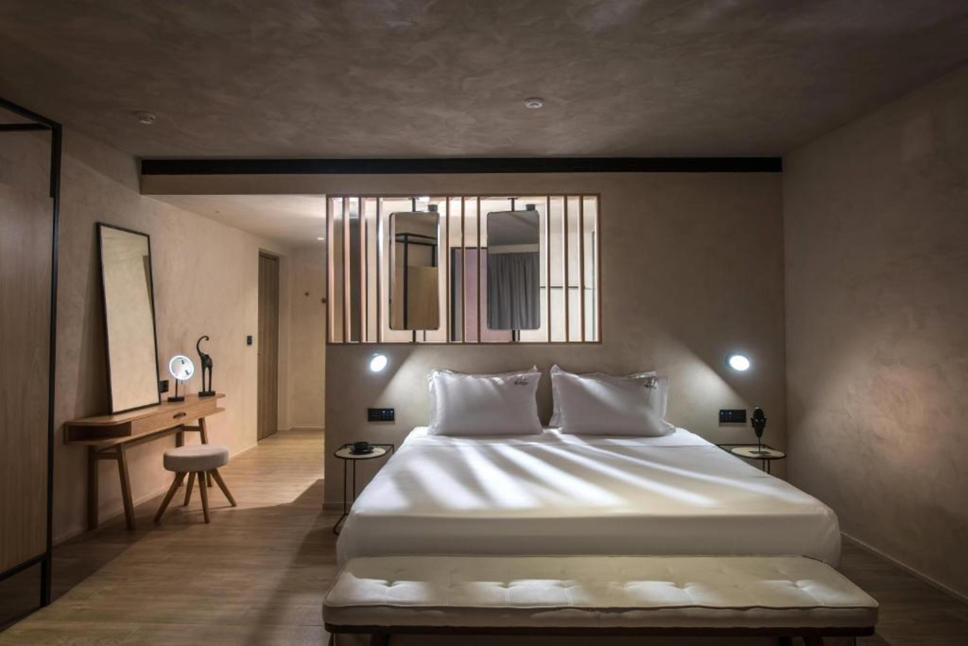 A modern bedroom with a large bed, bedside tables, a mirror, and a wall-mounted light fixture.