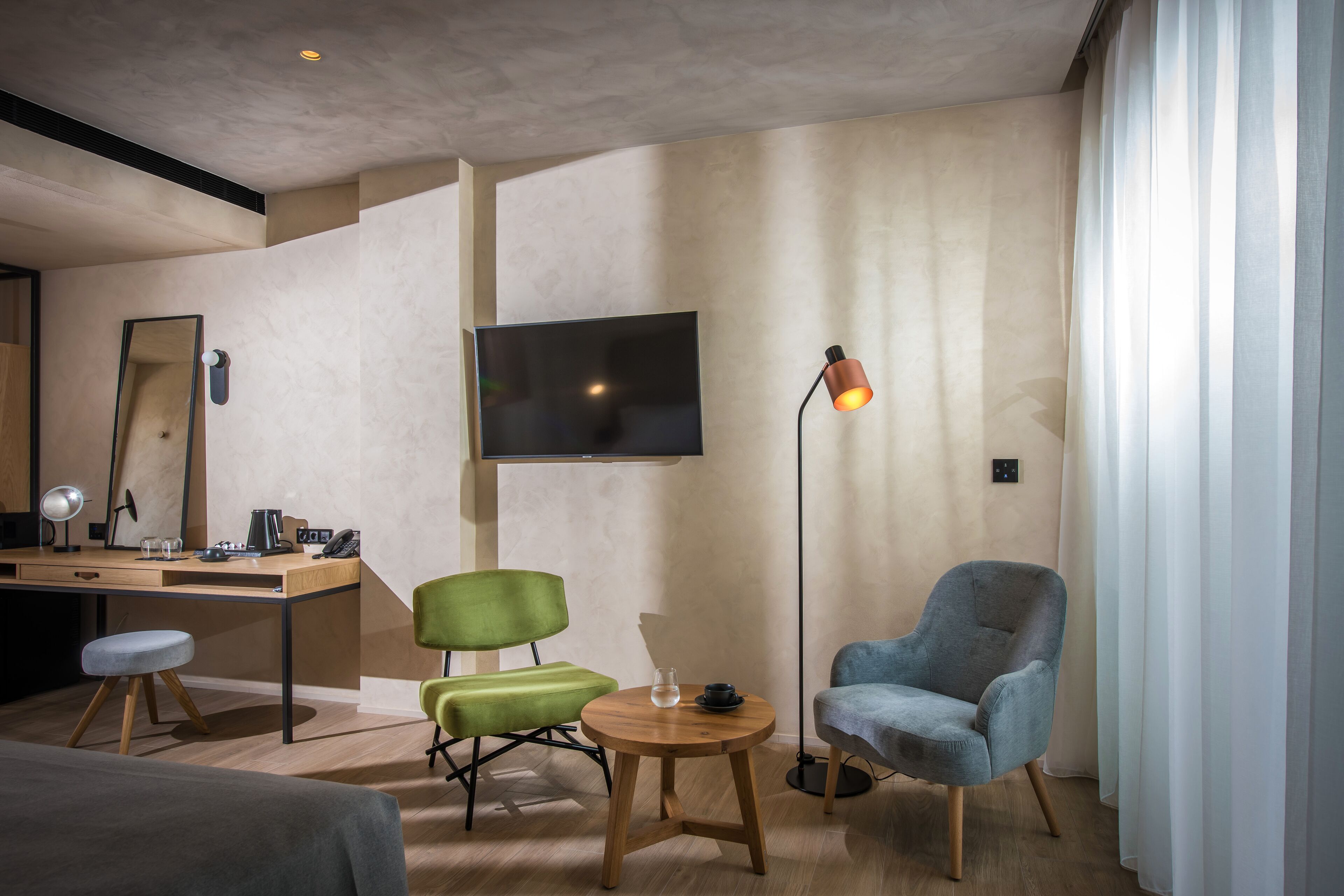Habitación de hotel moderna con un escritorio de madera, dos sillas, un televisor y una lámpara de pie.