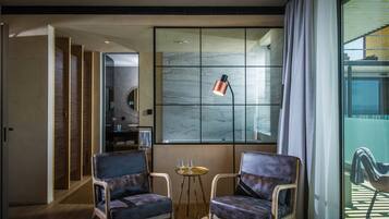 Una habitación moderna con dos sillones, una mesita con vasos y un ventanal con cortinas que ofrece vistas al exterior.