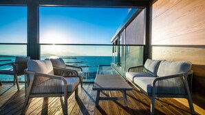 Terraza con mobiliario de mimbre y una mesa de cristal, con vista a un cuerpo de agua.