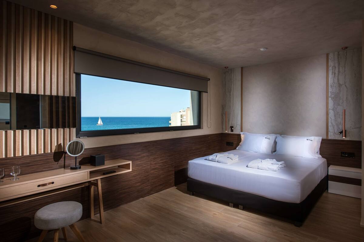 Una habitación de hotel moderna con un ventanal grande, una cama, un escritorio y un espejo.