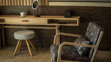 Una habitación moderna con un escritorio de madera, un taburete acolchado, un sillón de cuero, un espejo redondo pequeño y un control remoto.