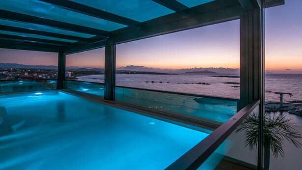 Una piscina infinita moderna con vista al océano y montañas distantes al atardecer.