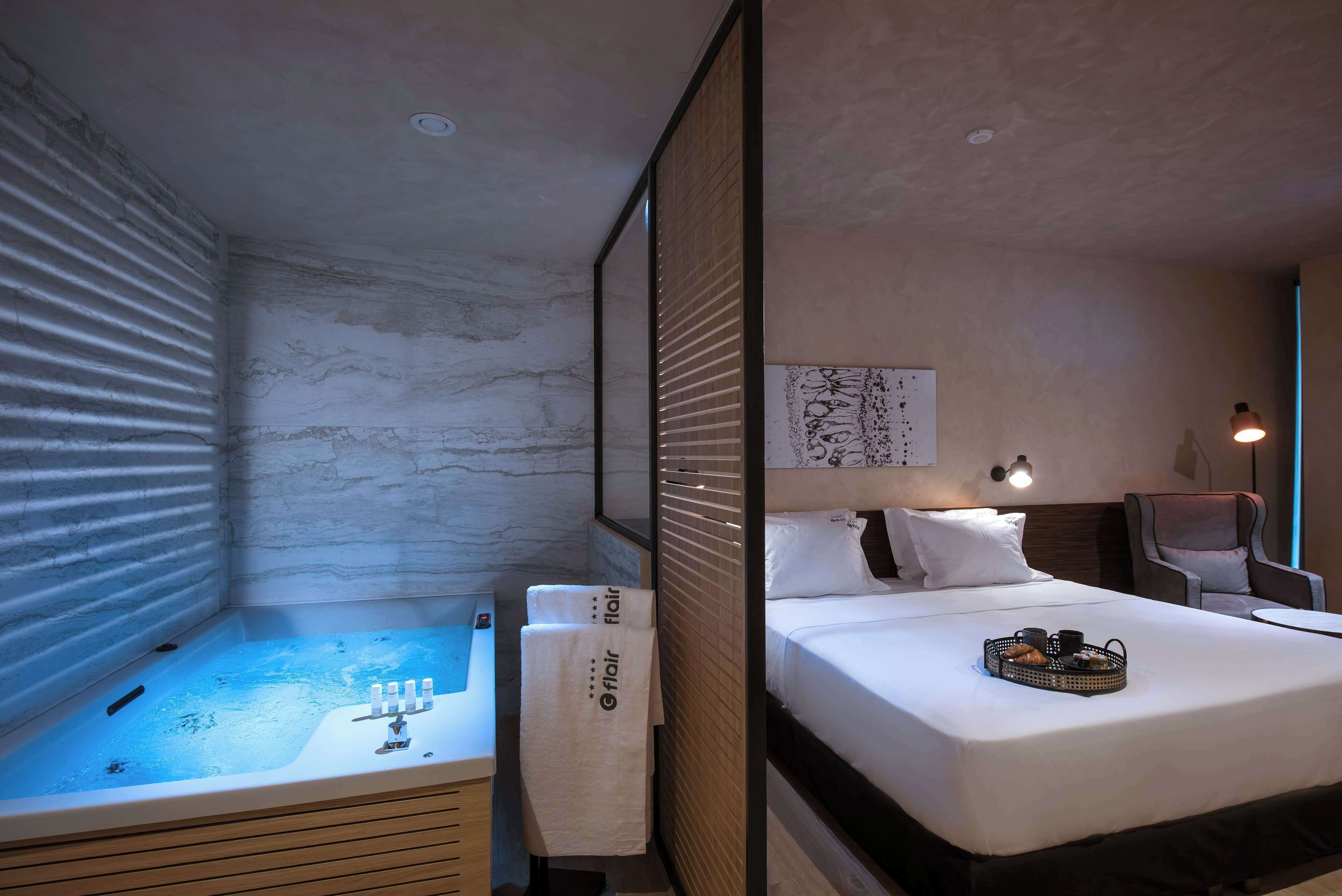 Quarto de hotel com uma cama grande, um pequeno espaço de estar, uma banheira e uma obra de arte na parede.
