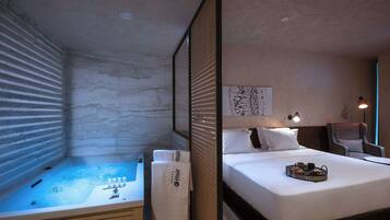 Quarto de hotel com uma cama grande, um pequeno espaço de estar, uma banheira e uma obra de arte na parede.