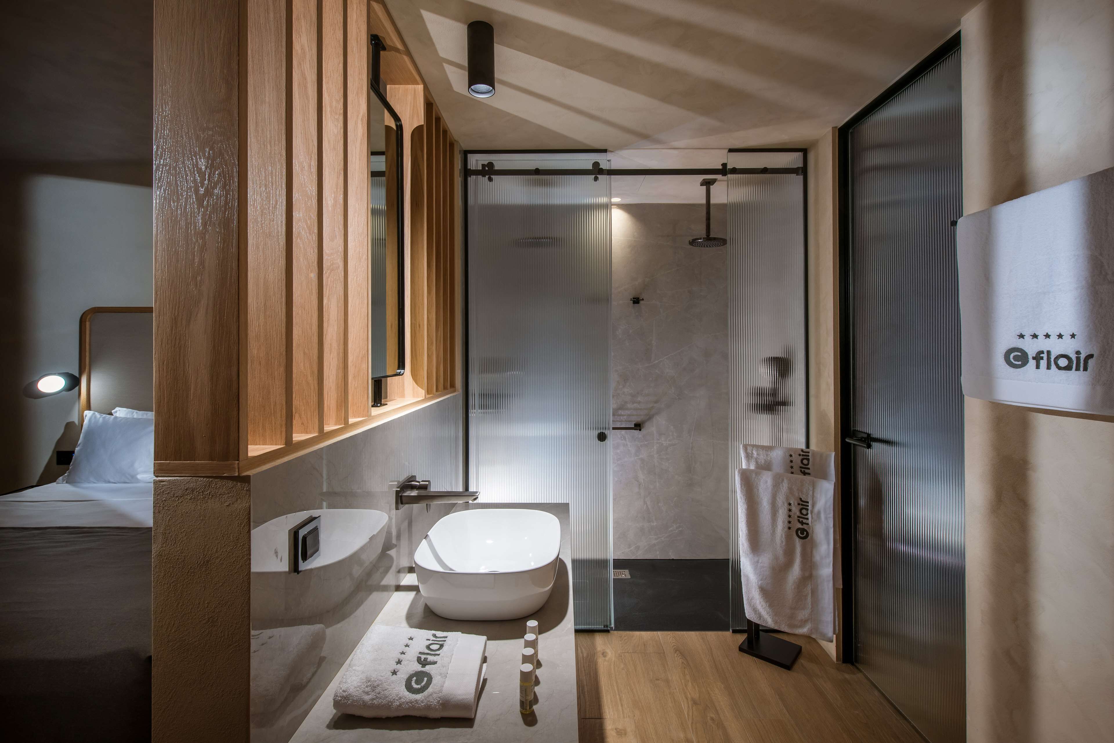 A modern bathroom with a wooden vanity, a large mirror, a freestanding bathtub, and a glass-enclosed shower area.