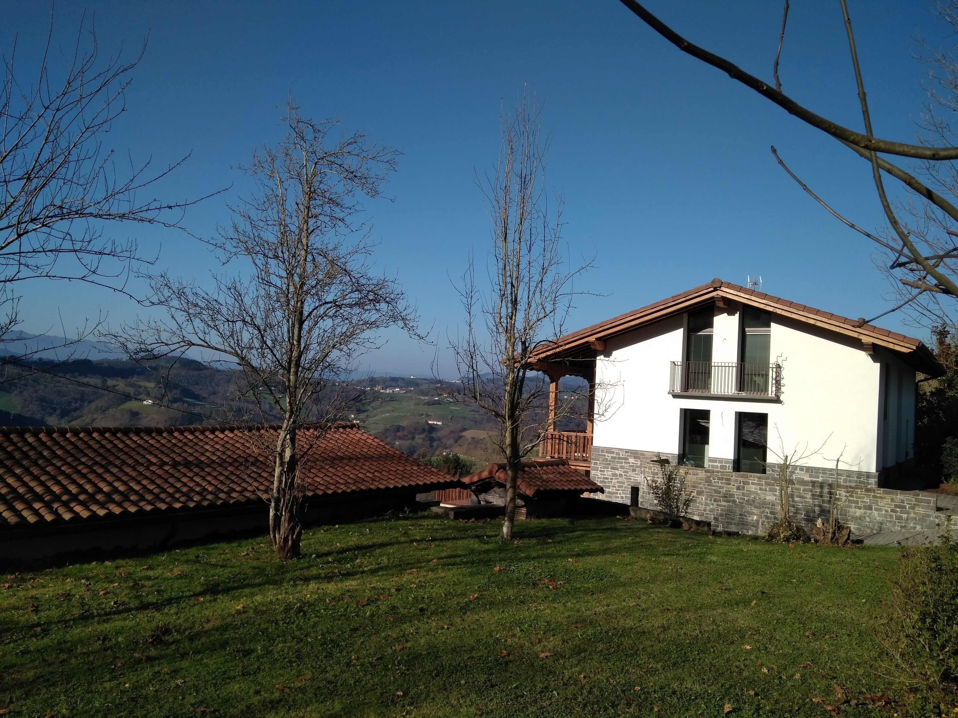 A two-story house with a balcony, surrounded by a grassy area and trees.