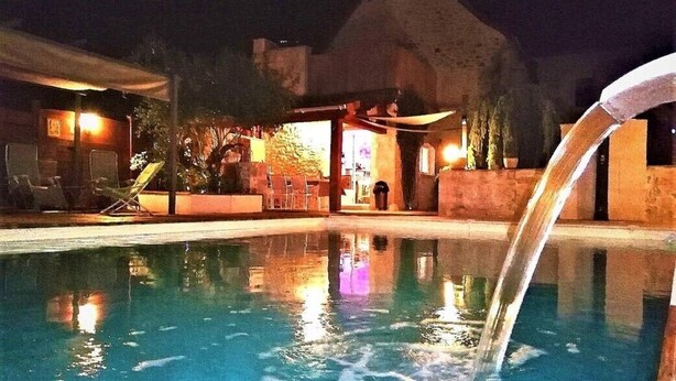A swimming pool with a waterfall feature, surrounded by lounge chairs and a covered area with seating.