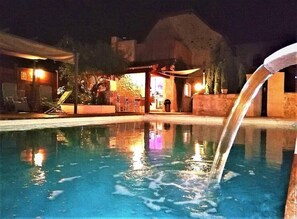 Uma piscina com uma cascata, rodeada por espreguiçadeiras e uma área coberta com assentos.