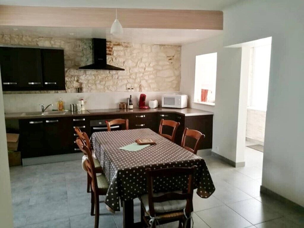 A modern kitchen with a stone wall, wooden cabinets, and a dining area with a table and chairs.