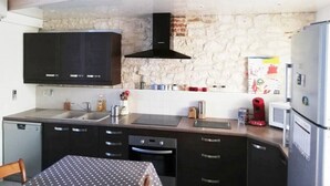 A compact kitchen with dark cabinets, a stone wall backsplash, a black range hood, and a refrigerator.