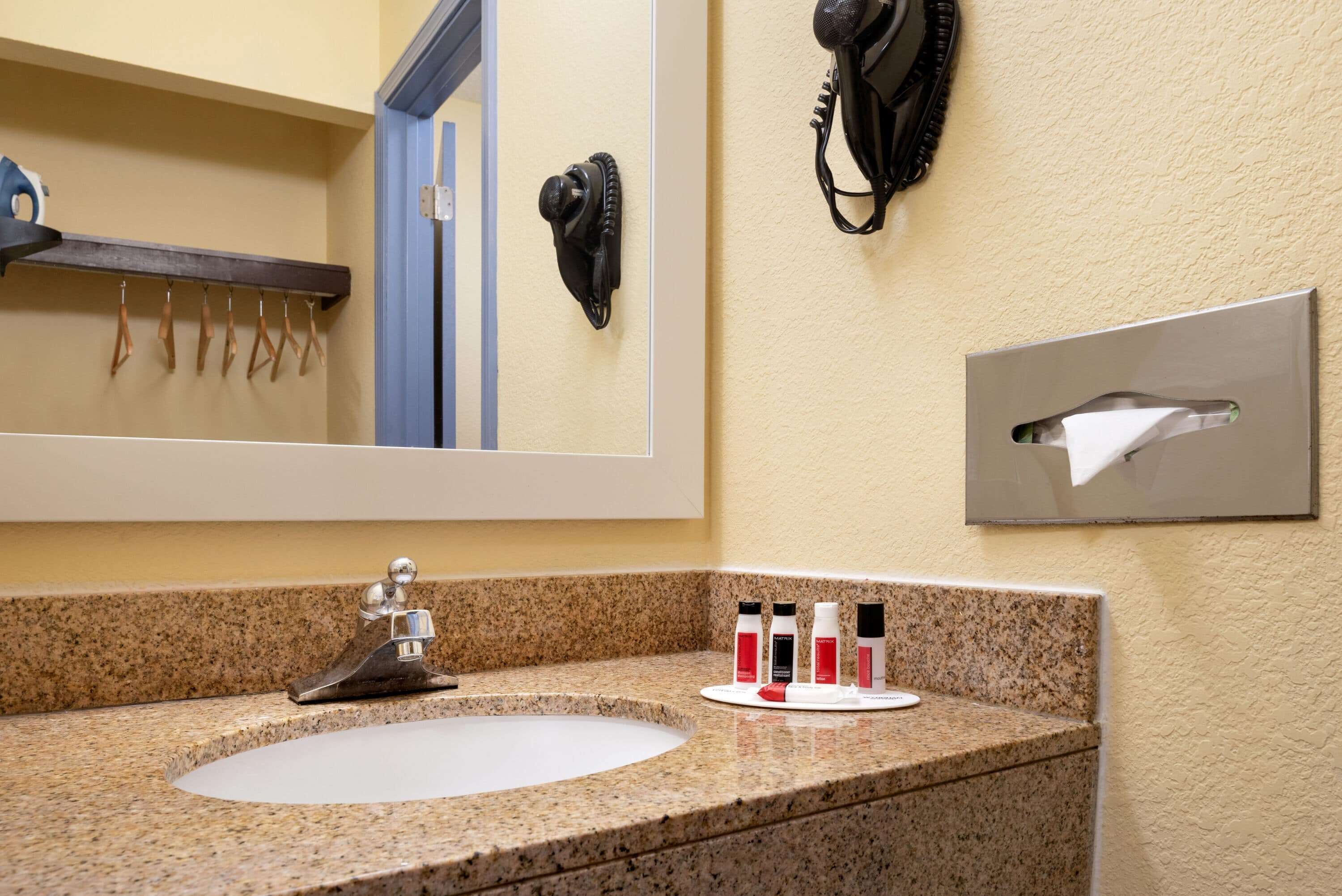 Baño con encimera de granito, lavamanos, espejo, teléfono y dispensador de toallas.